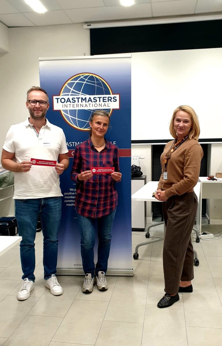 Uczestnicy spotkania z zakładkami „Welcome to Toastmasters” przed banerem klubu